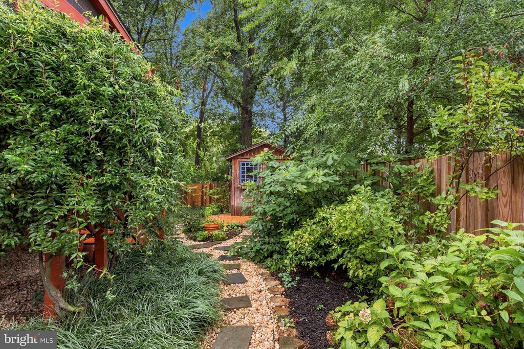 Landscaped backyard with a stepping-stone path winding through greenery to a wooden garden shed.