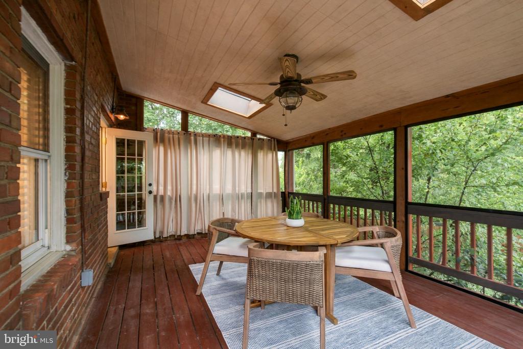 Covered porch with a round dining table and wicker chairs overlooking leafy trees.