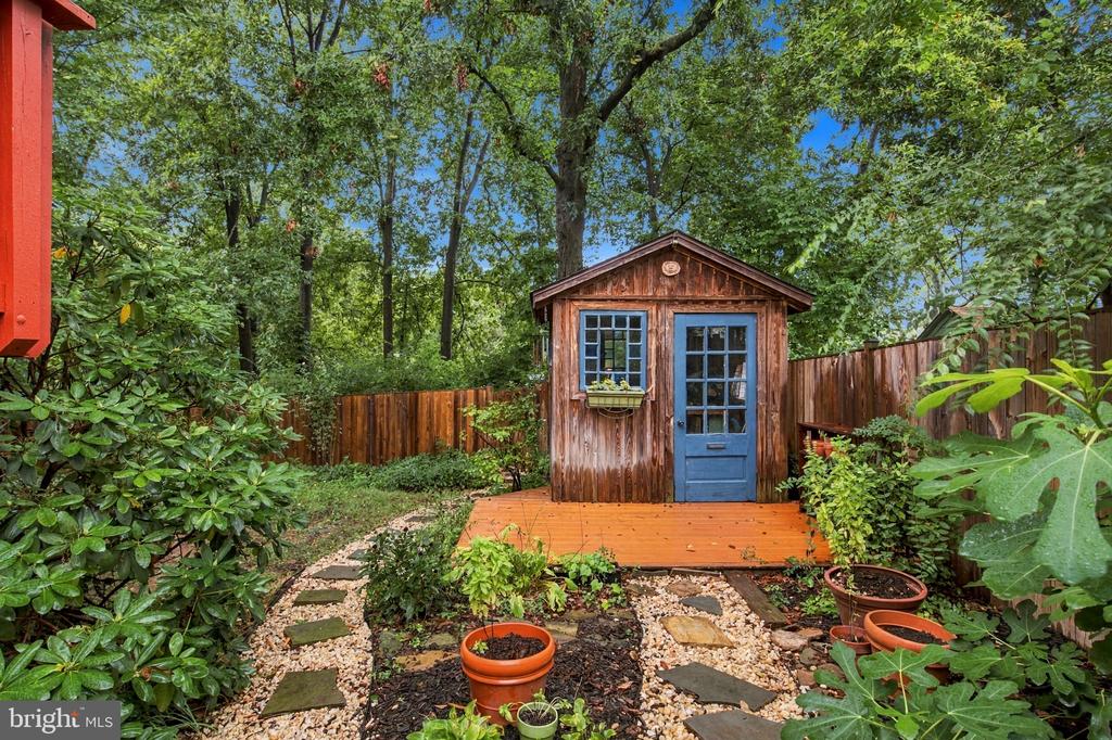 Backyard shed with a blue door, raised deck, stepping-stone path, and surrounding garden.