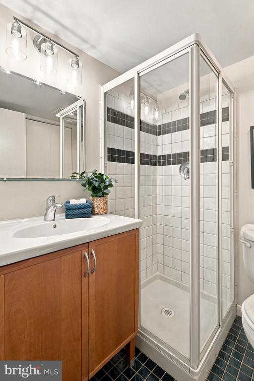 Bathroom with a glass shower featuring black tile bands beside a wood vanity and white sink.