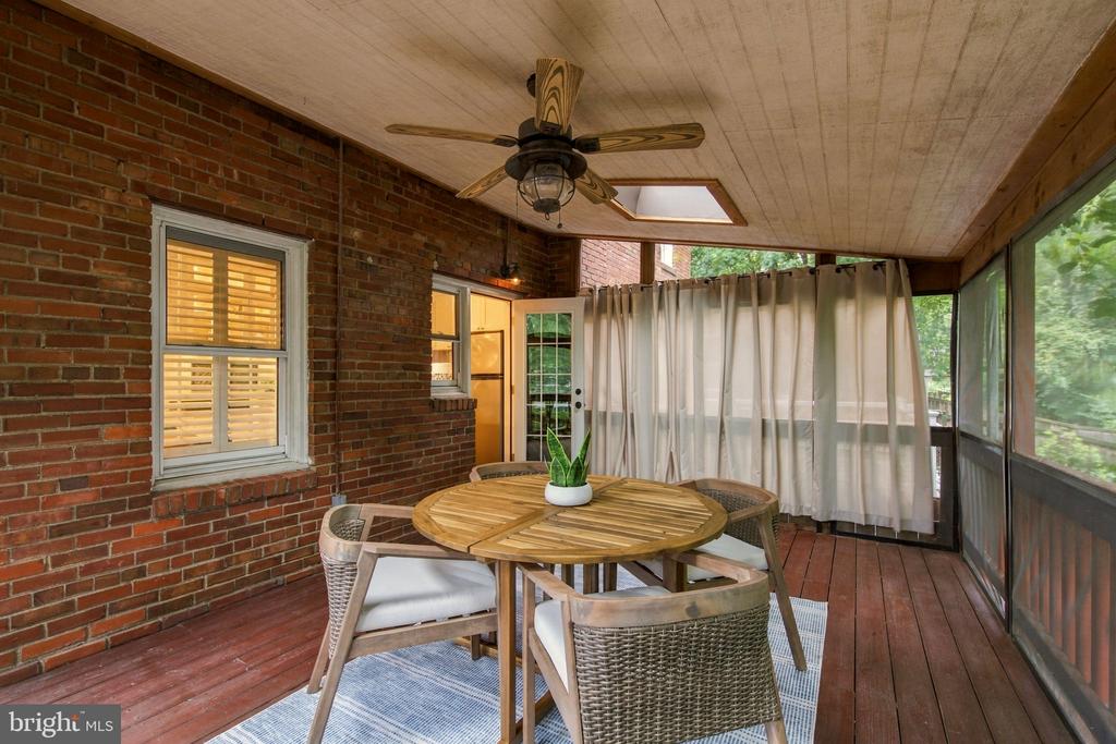 Screened-in porch with a round dining table, wicker chairs, and brick walls.
