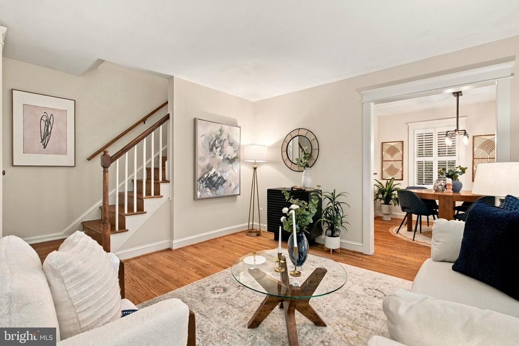 Living room with white sofas, a glass coffee table, hardwood floors, and an adjoining dining area.