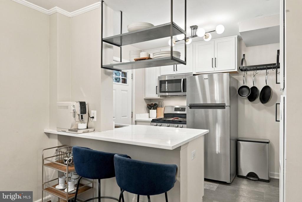 Kitchen with stainless steel appliances, white peninsula, two navy stools, and hanging open shelves.