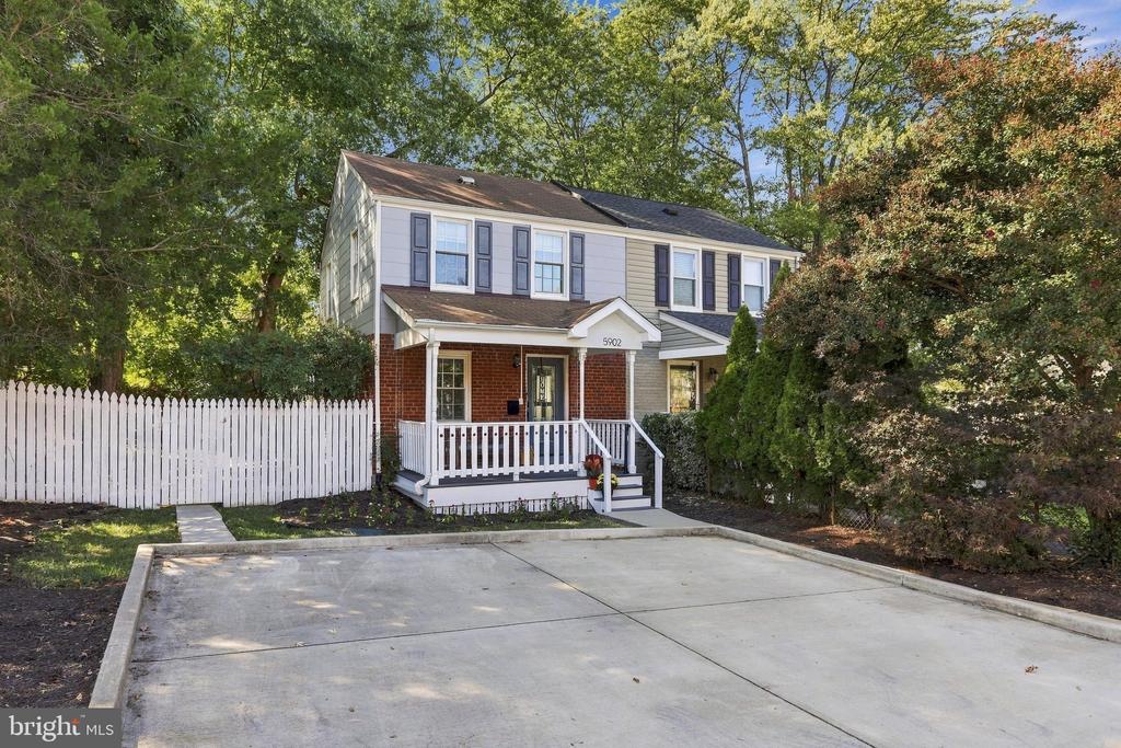 Two-story brick and siding house with a covered porch, wide concrete driveway, and white picket fence.