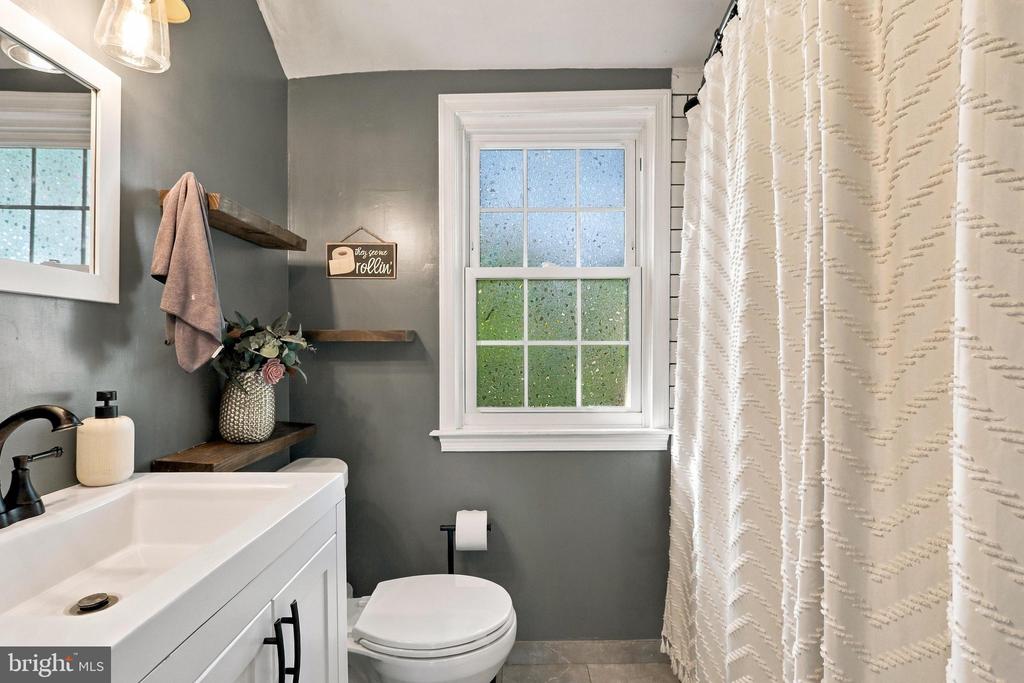 Bathroom with a white vanity, gray walls, floating shelves, and a patterned shower curtain.