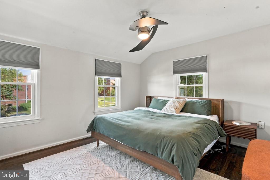 Bedroom with a wooden bed in green bedding, three windows, and a ceiling fan with light.