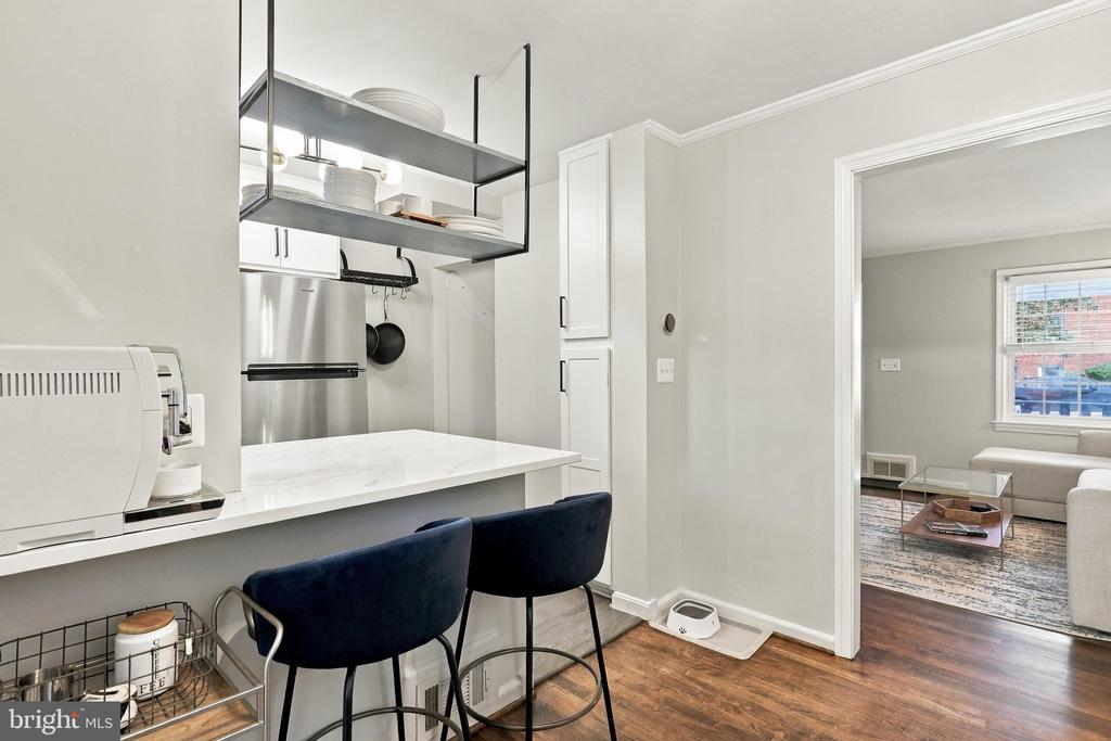 Kitchen with a white breakfast counter, dark blue stools, and open shelving beside the living room.