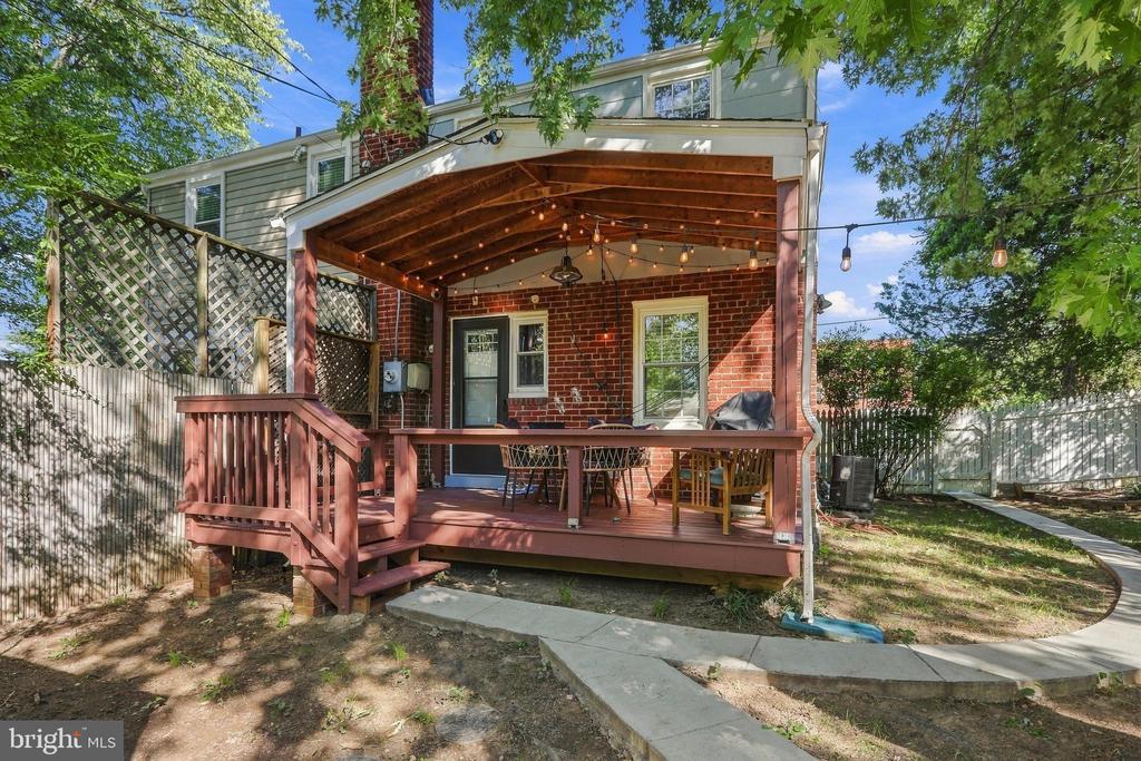Home’s covered brick patio with a raised wood deck, outdoor dining set, and string lights.