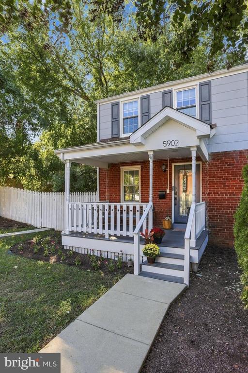 Two-story house with a brick lower facade, covered white porch, and picket fence.