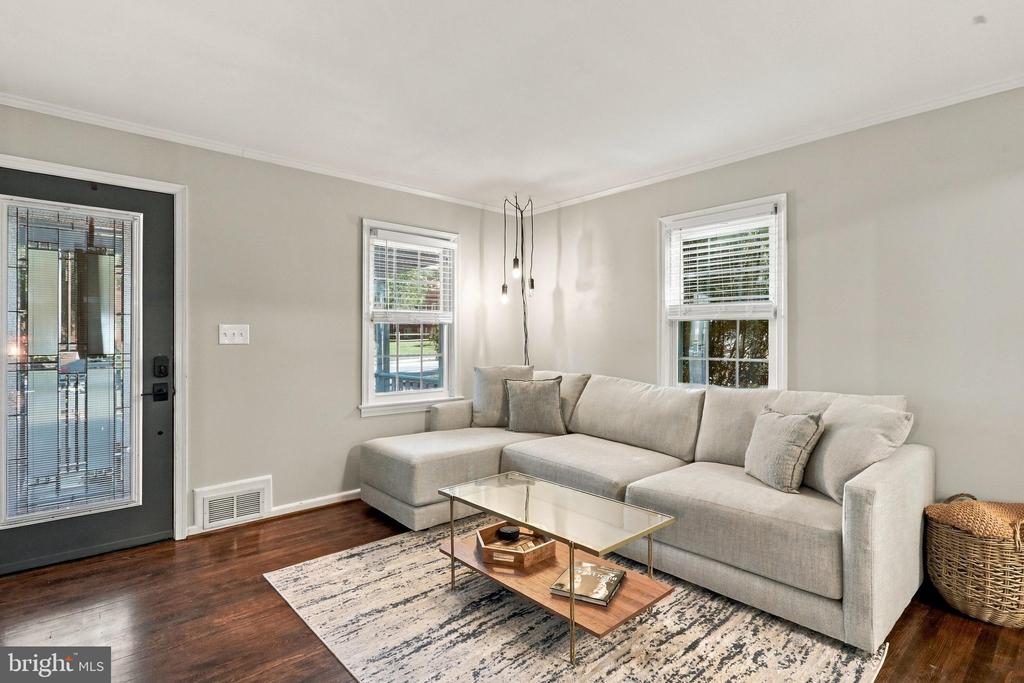 Living room with a gray sectional, glass coffee table, patterned rug, and dark hardwood floors.