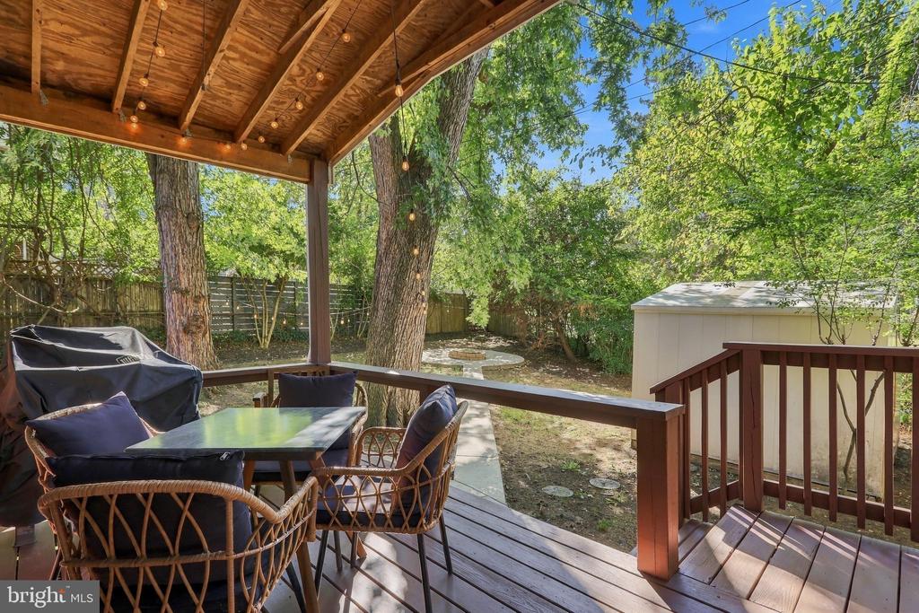 Covered backyard deck with wicker seating, string lights, mature trees, and a garden shed.