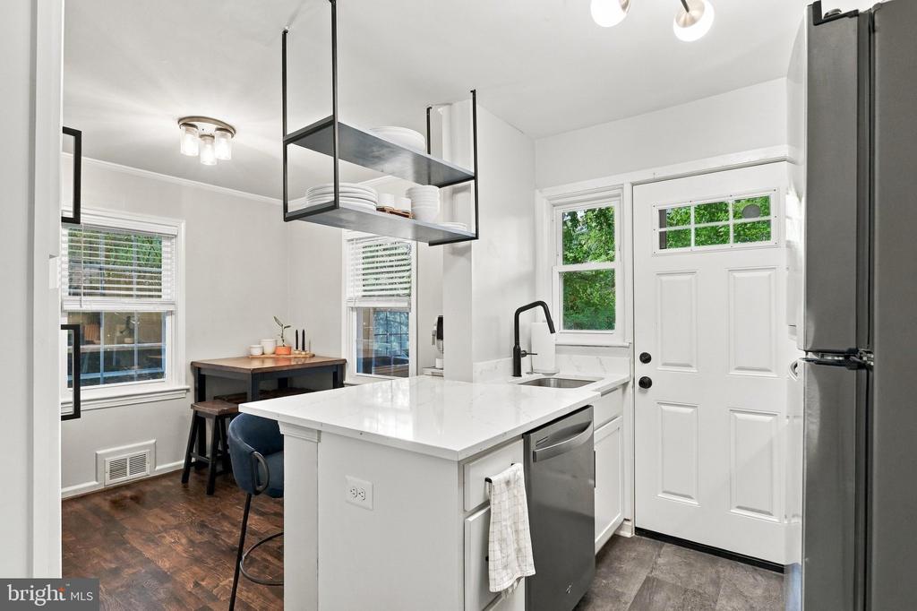 Bright kitchen with a white quartz island, black open shelving, and a back door beside leafy windows.