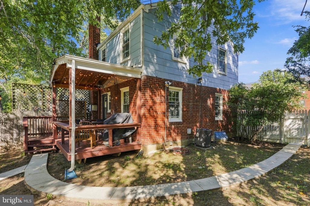 Rear of a brick-and-blue house with a covered deck, string lights, and a curved concrete path.