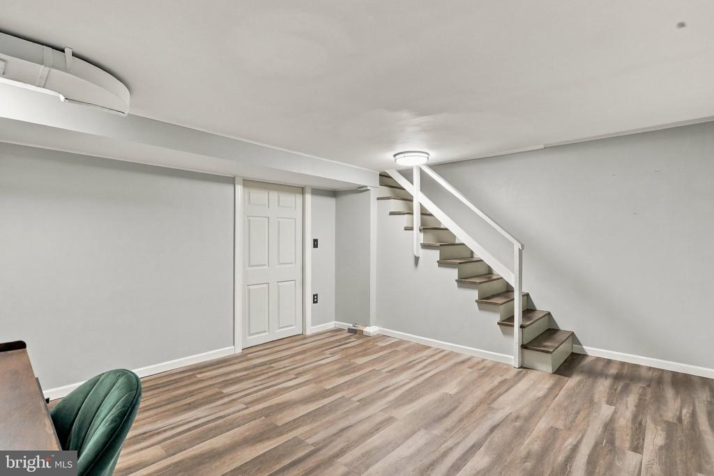 Finished lower-level room with wood-look flooring and stairs with a white railing.