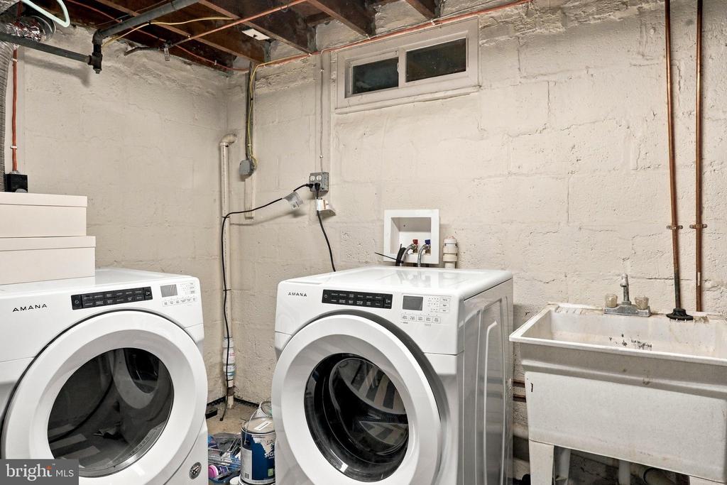 Basement laundry room with two front-loading machines and a deep utility sink.