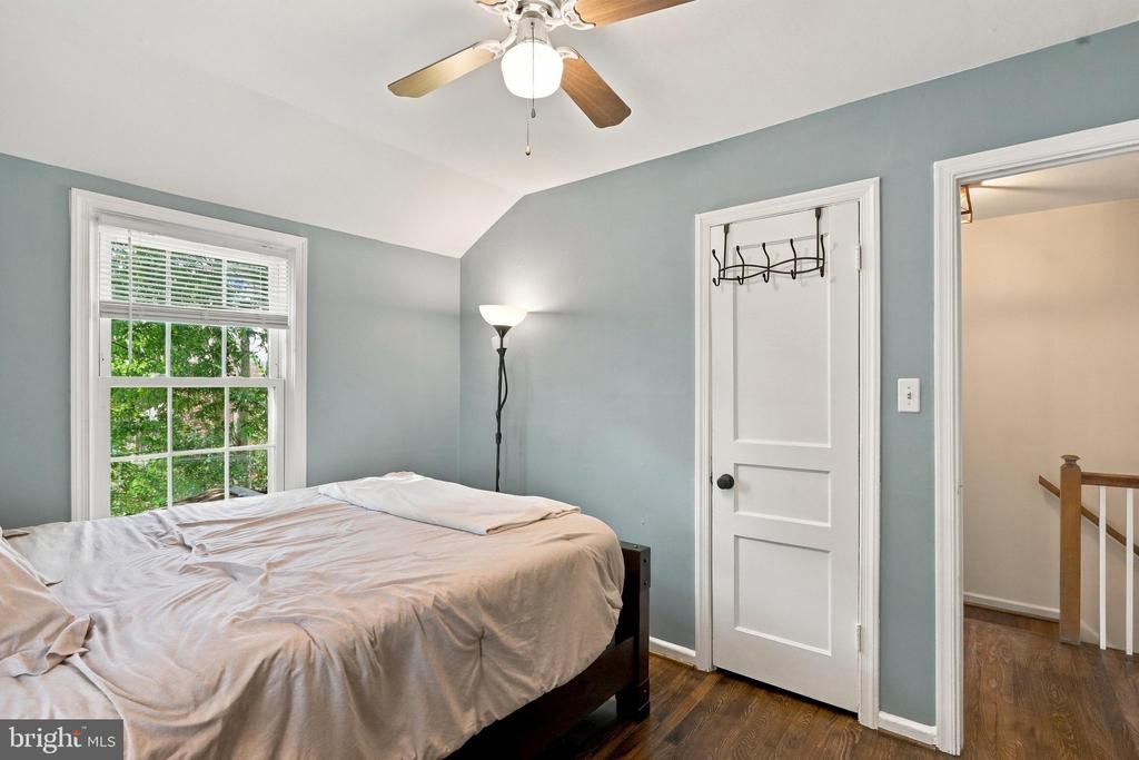 Bedroom with a bed, ceiling fan, and window overlooking green trees.