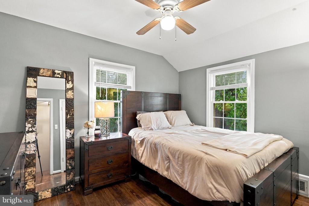 Bedroom with a dark wood bed, hardwood floors, two windows, and a ceiling fan.