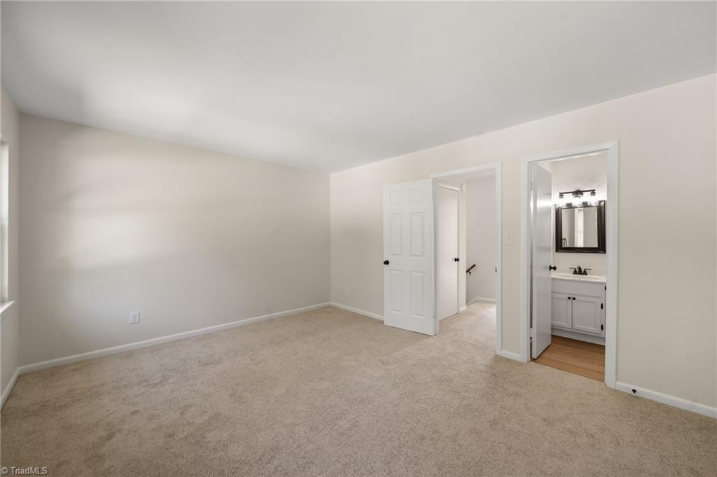Empty carpeted bedroom with an open doorway to a bathroom vanity and mirror.