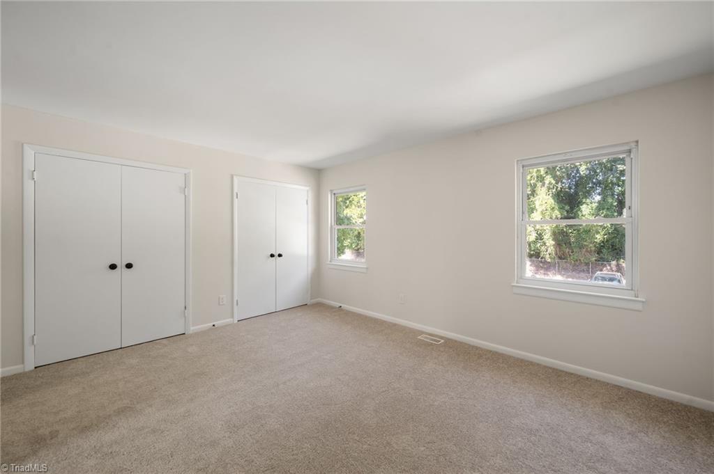 Empty bedroom with beige carpet, two closets, and windows overlooking trees.