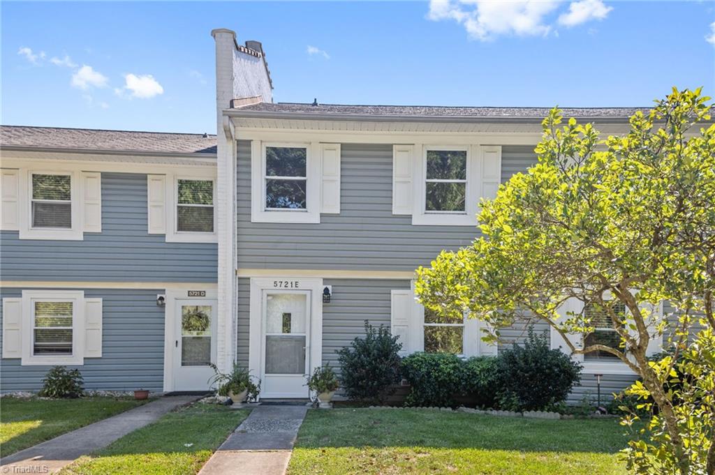 Gray two-story attached home with white shutters, front walkway, and leafy tree.