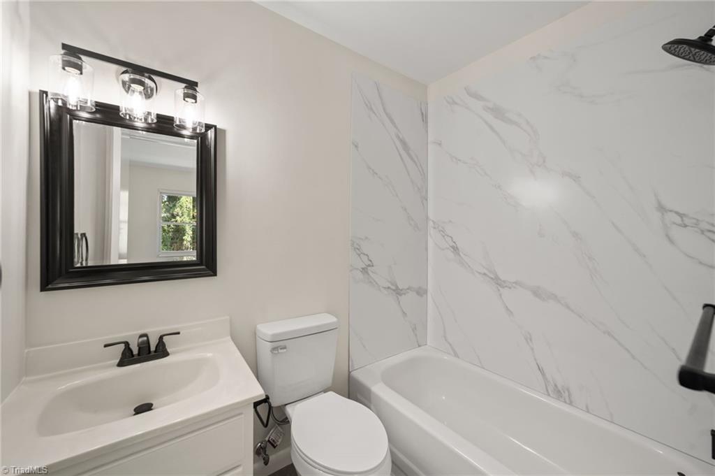 Bathroom with a white vanity, black-framed mirror, and bathtub surrounded by marble-look wall panels.