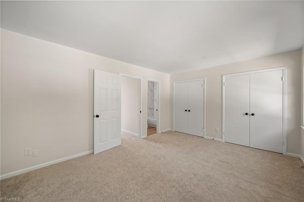 Vacant bedroom with beige carpet, two white closets, and an open doorway to a bathroom.