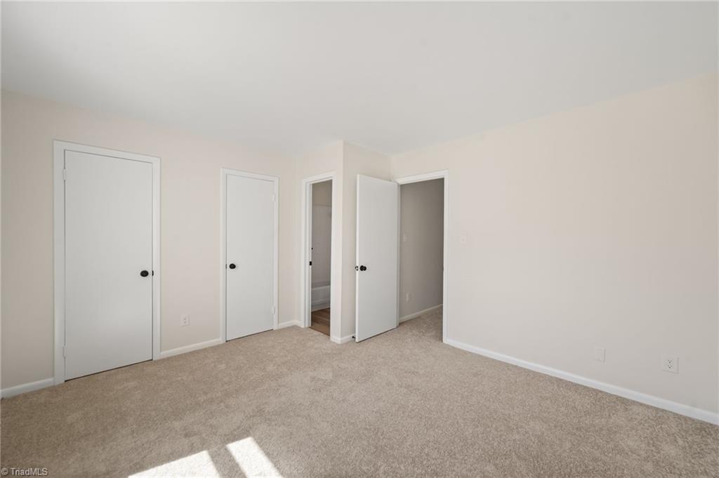 Empty bedroom with beige carpet and several white doors, one open.