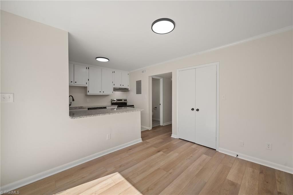 Vacant kitchen with white cabinets, granite peninsula, and light wood flooring.