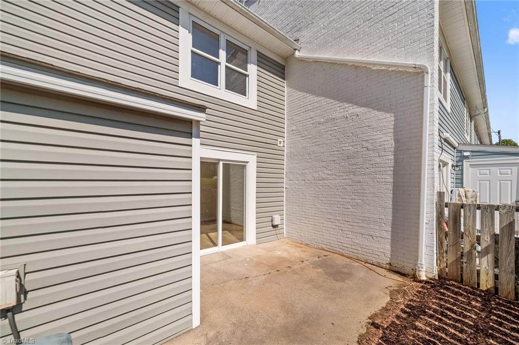 Concrete patio beside a townhouse with gray siding, sliding glass door, and brick wall.