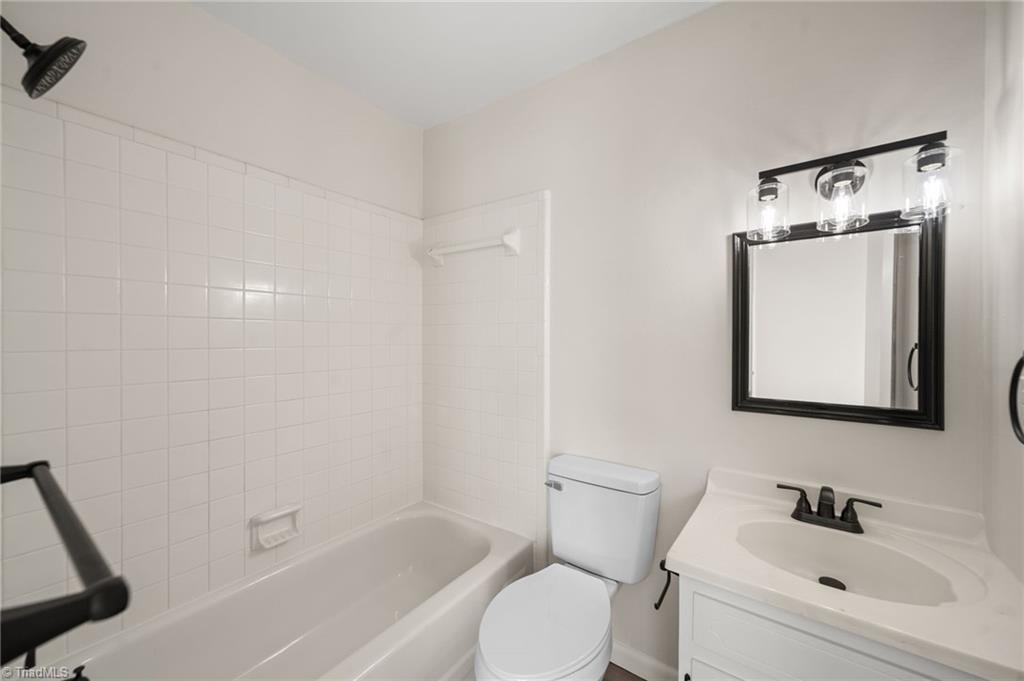 Bathroom with tiled bathtub, toilet, and white vanity beneath a black-framed mirror.