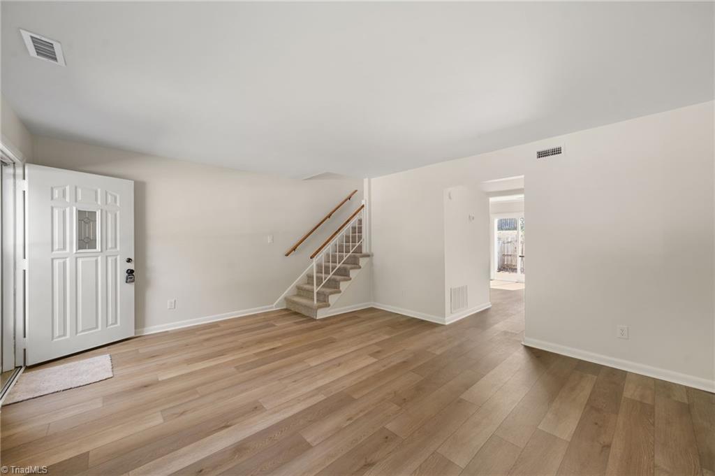 Empty entryway with wood-look floors, a white front door, and carpeted stairs.