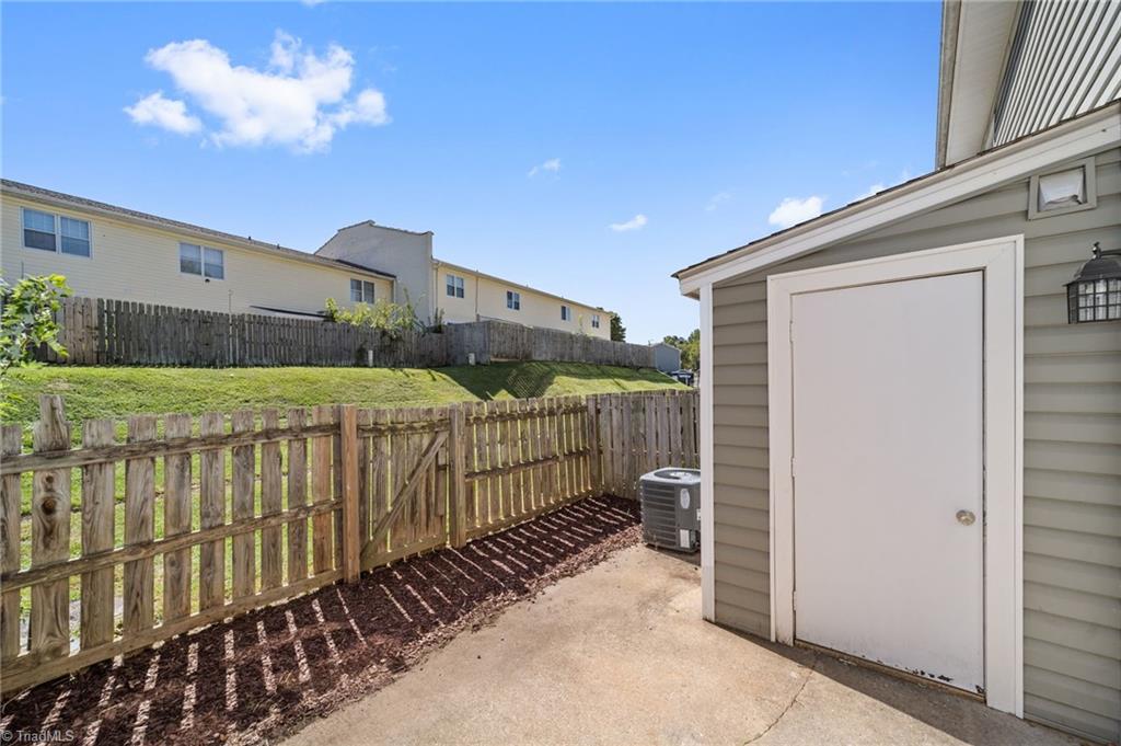 Concrete patio beside a white exterior door, with a wooden fence and air-conditioning unit.