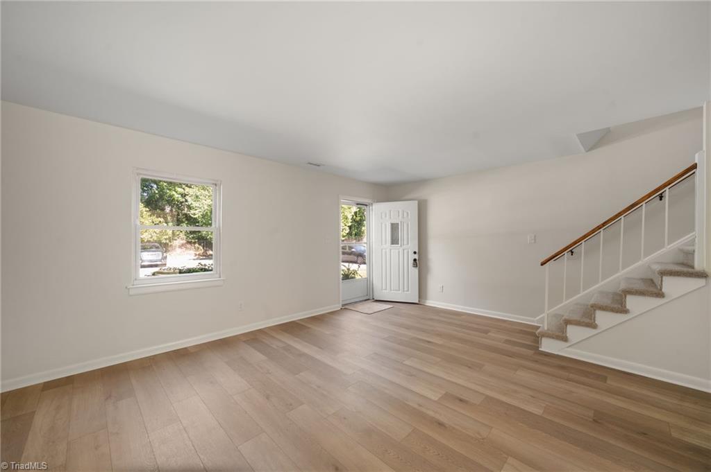 Vacant living area with light plank flooring and a staircase beside the front door.