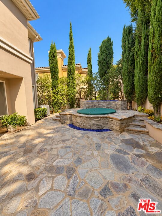 Raised circular spa in a stone-paved backyard patio surrounded by tall cypress trees.