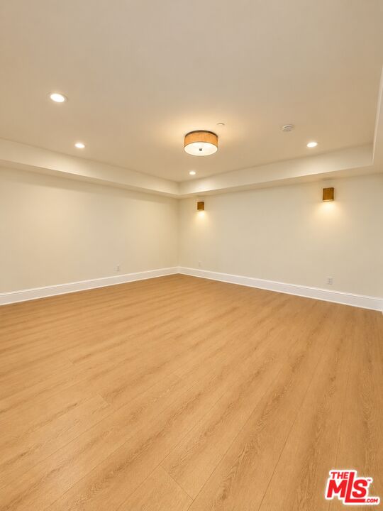 Empty room with light wood floors, a recessed tray ceiling, and warm lighting.