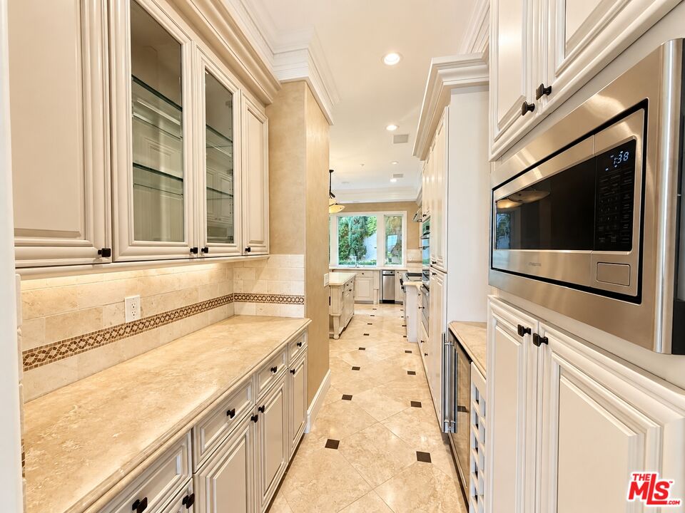 Long cream kitchen with glass-front cabinets, stone counters, and a built-in stainless steel microwave.