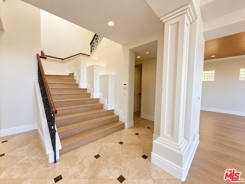 Foyer with a broad wood staircase, wrought-iron railing, and stone tile floor.