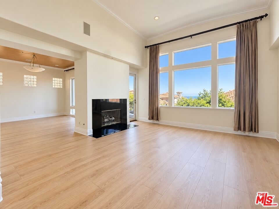 Vacant living room with a black fireplace and tall windows overlooking rooftops and the ocean.