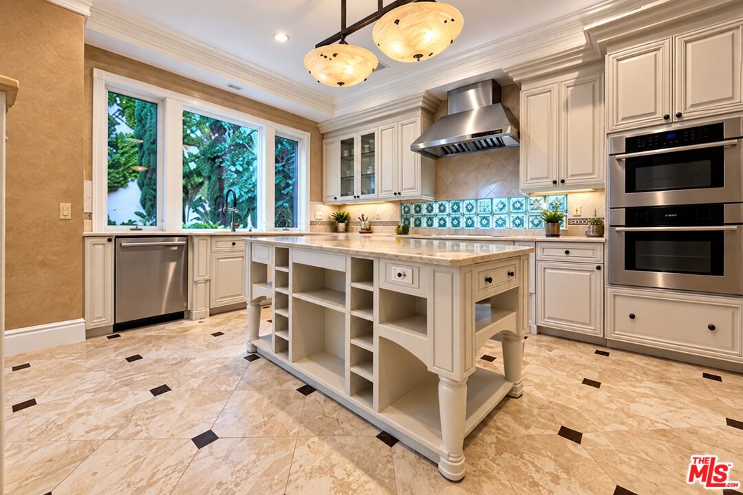 Kitchen with a large cream island, blue patterned backsplash, and windows overlooking greenery.