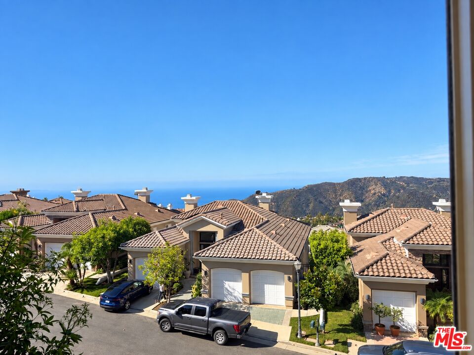 Neighborhood of tile-roof homes with ocean and coastal mountains in the distance.