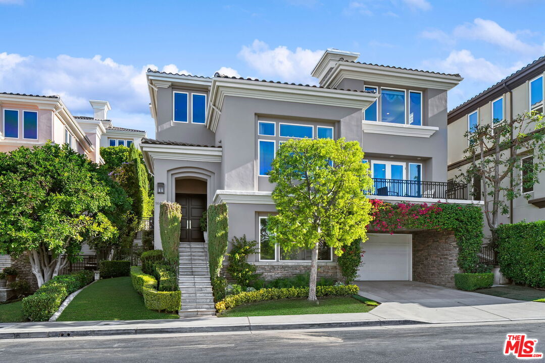 Gray two-story home with white trim, a front staircase, landscaped garden, and attached garage.