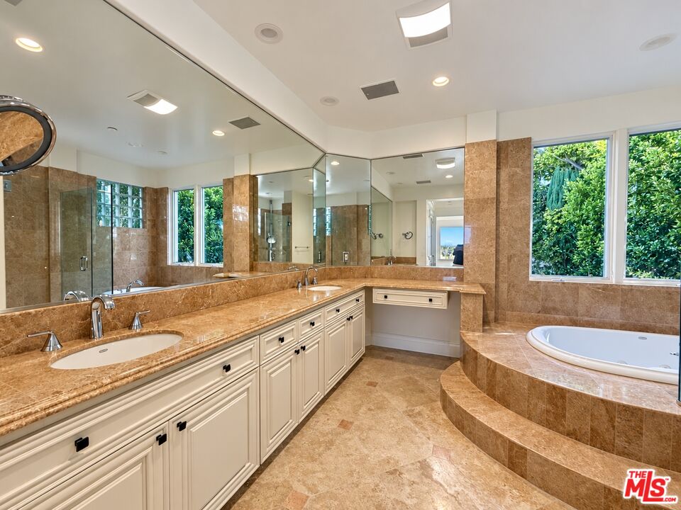 Spacious bathroom with a double vanity and raised soaking tub beside windows overlooking greenery.