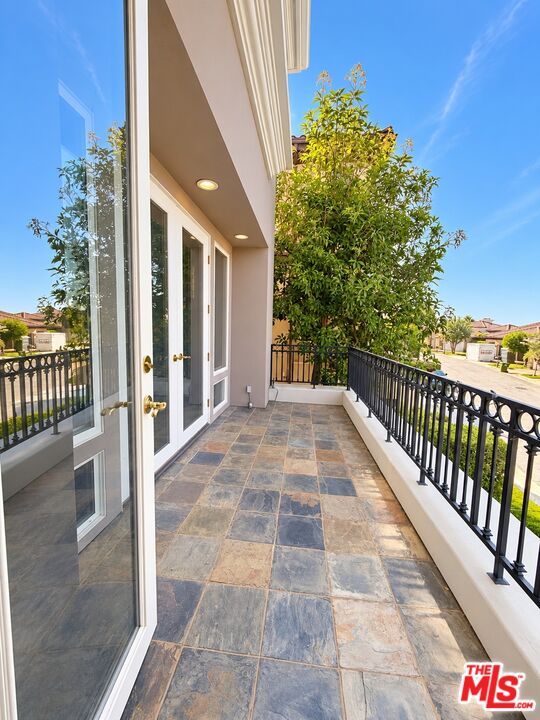 Second-floor balcony with stone tile, black railings, and glass French doors beside a leafy tree.