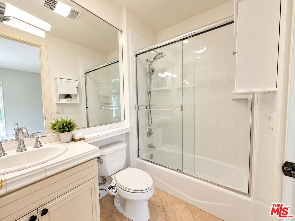 Bathroom with a cream vanity, large mirror, and glass-enclosed bathtub and shower.