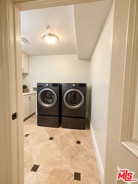 Laundry room with black front-loading washer and dryer, white cabinetry, and beige tile flooring.