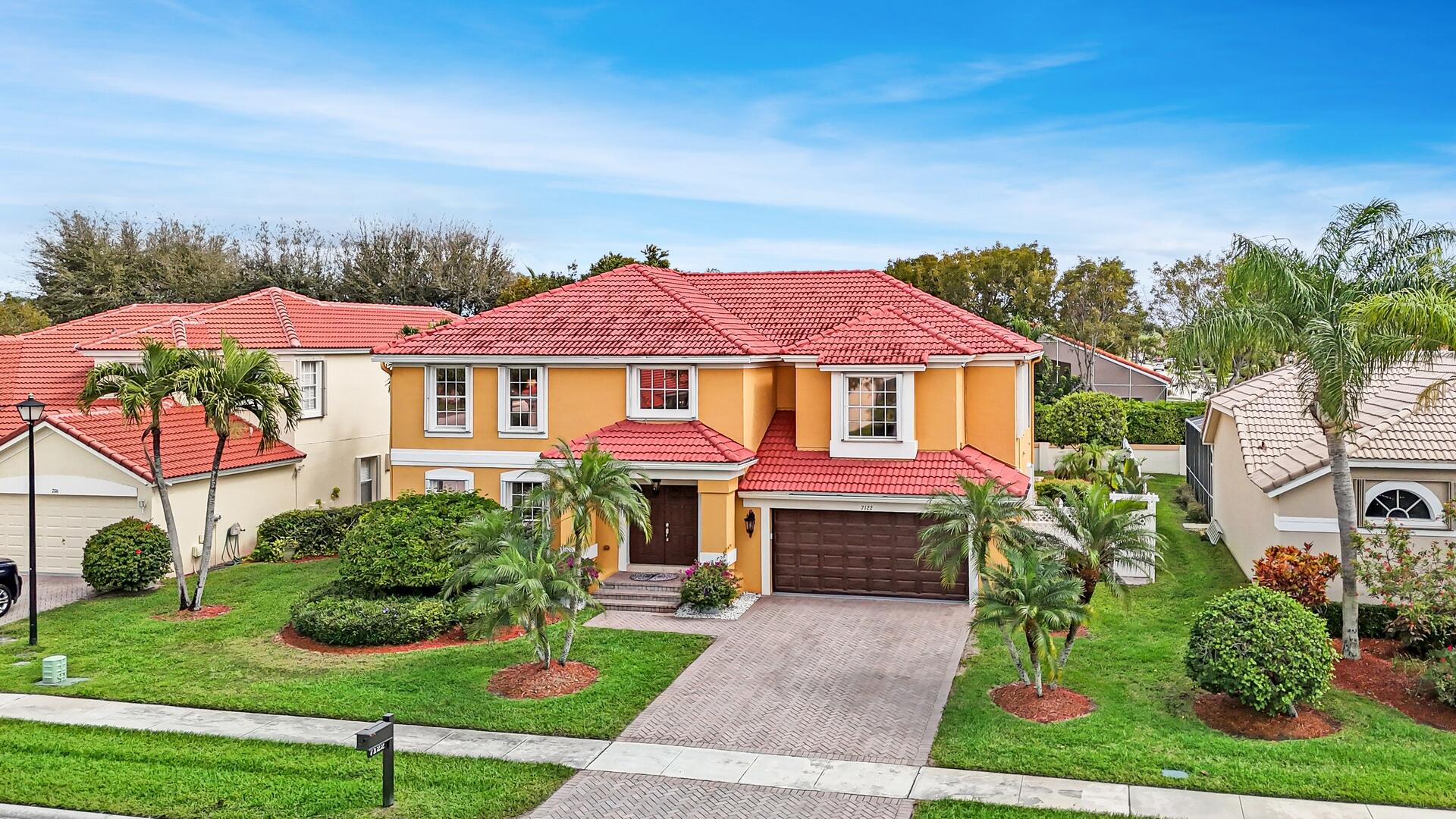 Two-story orange home with a red tile roof, double garage, paver driveway, and landscaped palms.