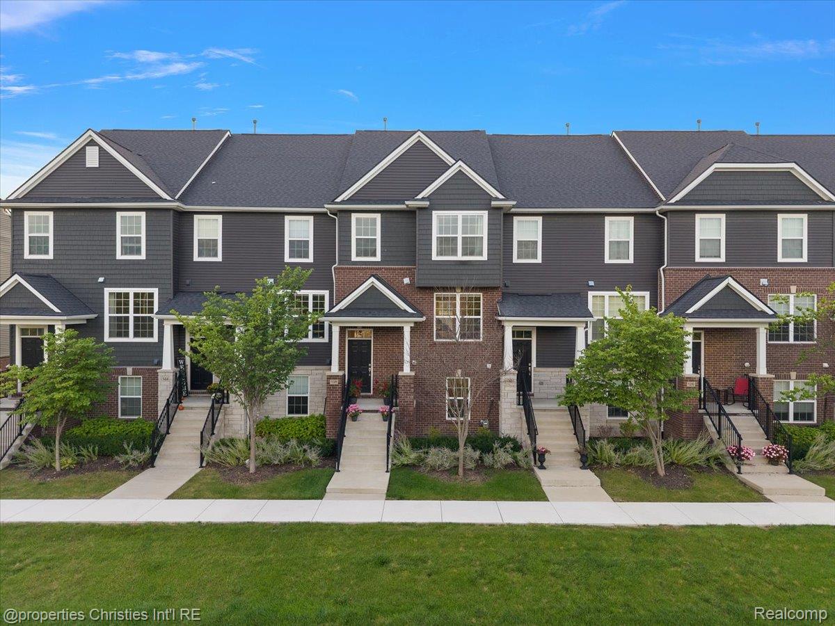 Row of gray and brick townhomes with peaked roofs, front porches, and landscaped entrances.