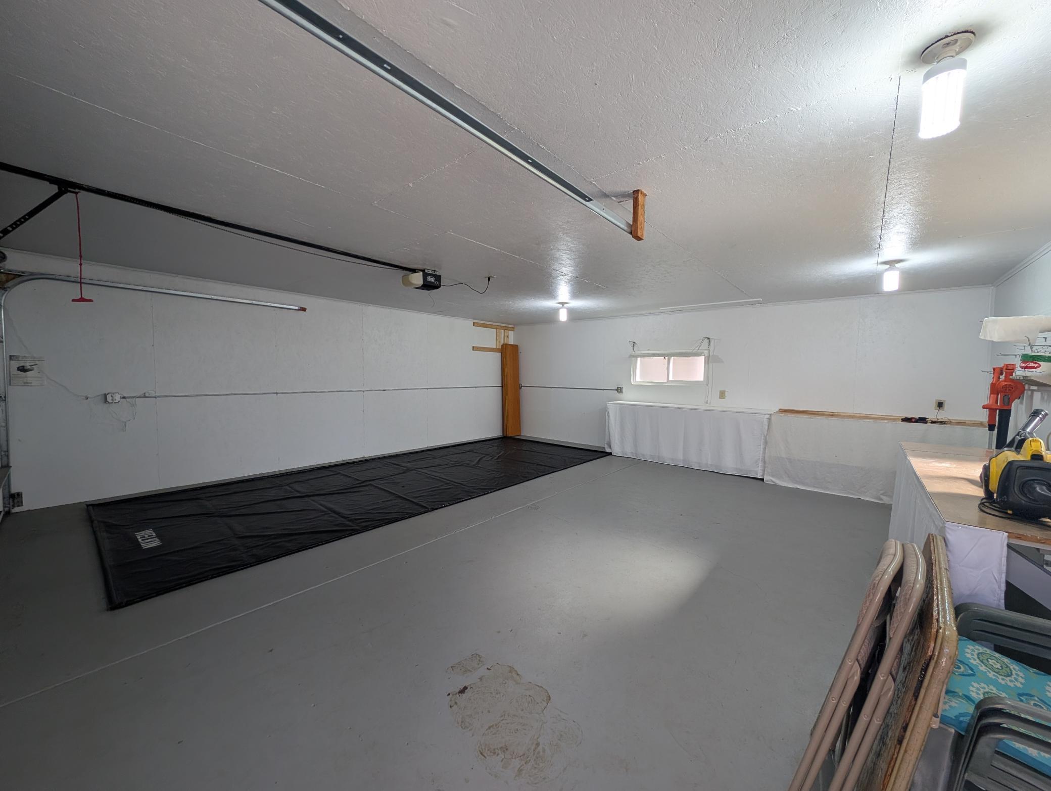 Spacious garage with overhead door tracks, a small window, and work surfaces along one wall.