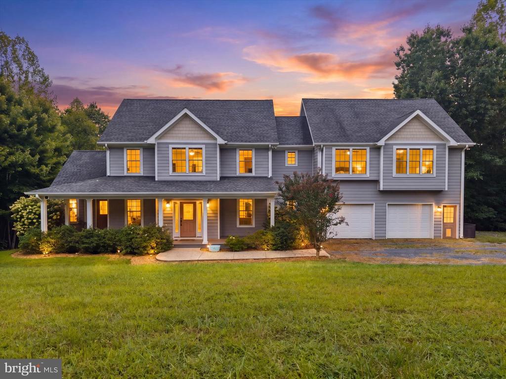 Gray two-story house with a covered porch and glowing windows at dusk.