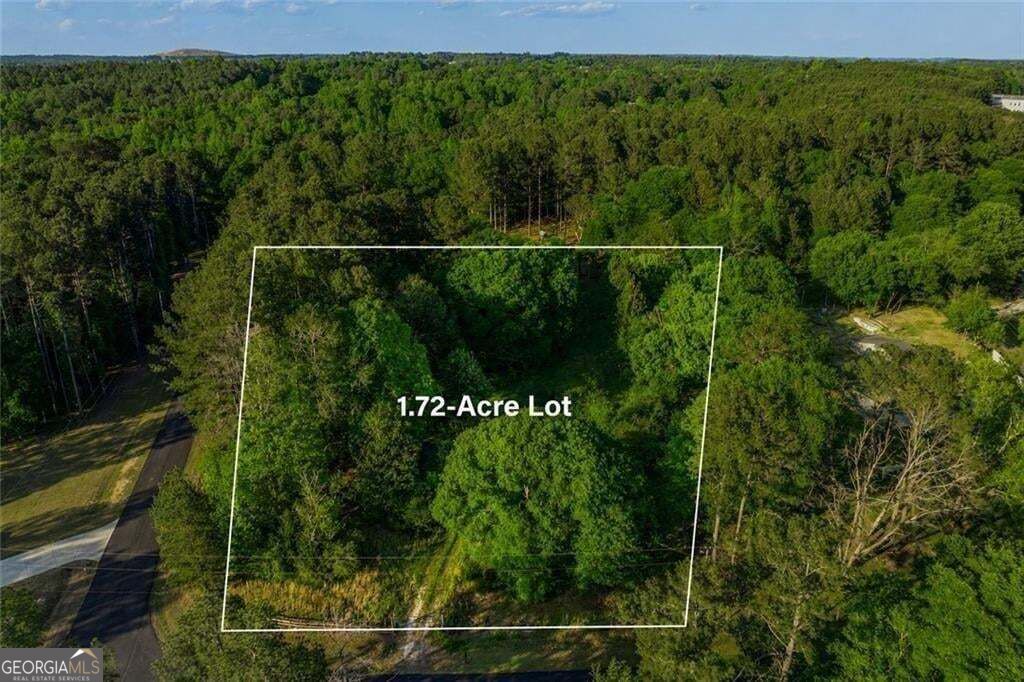 Aerial view of a wooded 1.72-acre lot outlined beside a paved road.